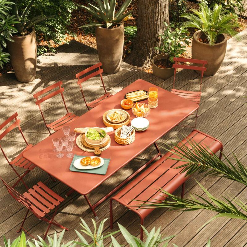 Fermob Outdoor-Essgruppe in Terrakotta-Rot – stilvolle Gartengarnitur mit Tisch, Stühlen und Bank auf Holzterrasse, ideal für sommerliche Gartenpartys im Grünen