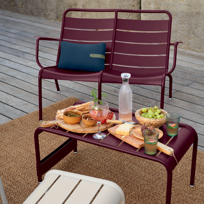 Fermob Luxembourg tiefer Sessel in burgunderrot – stilvolle Gartenlounge mit Beistelltisch, Getränken und Snacks auf Holzterrasse für gemütliche Outdoor-Momente
