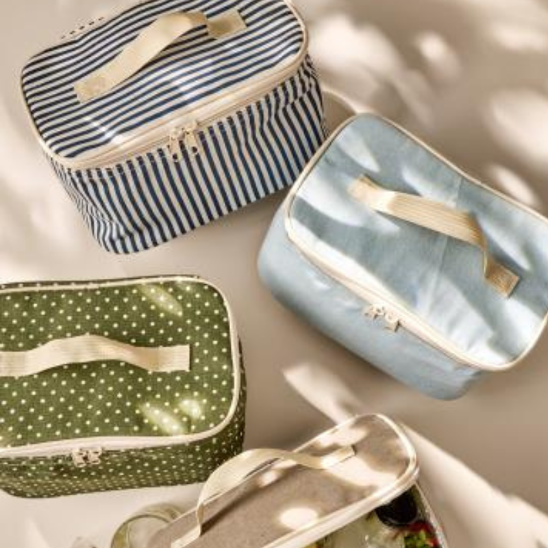 Vier Kühltaschen in verschiedenen Farben dekorativ arrangiert auf hellem Untergrund mit Sonnenlicht und Schattenspiel